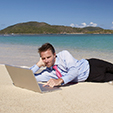 Relaxed businessman relaxing on tropical beach with his feet in the water surfing the internet on a laptop